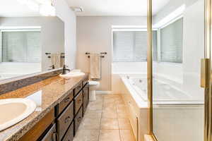 Bathroom featuring a jetted tub, double vanity, light tile patterned floors, and healthy amount of natural light
