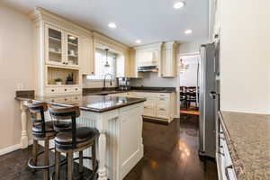 Kitchen featuring dark stone countertops, a kitchen bar, pendant lighting, glass insert cabinets, and a peninsula