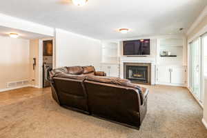 Living room featuring built in shelves, a tiled fireplace, crown molding, washer / dryer, and light carpet