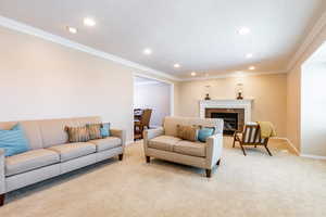 Carpeted living area featuring crown molding, a tiled fireplace, and recessed lighting