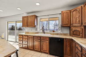 Kitchen featuring brown cabinets, black dishwasher, light countertops, recessed lighting, and light tile patterned floors