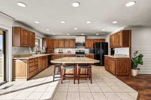 Kitchen featuring brown cabinets, a breakfast bar, black appliances, recessed lighting, and a kitchen island