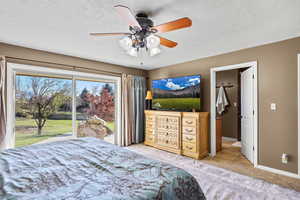 Master Bedroom with access to exterior, light colored carpet, a ceiling fan, and a textured ceiling