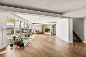 Unfurnished living room featuring a lit fireplace, wood finished floors, a textured ceiling, and stairway