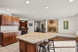 Kitchen featuring light countertops, light tile patterned floors, a glass covered fireplace, brown cabinetry, and a center island