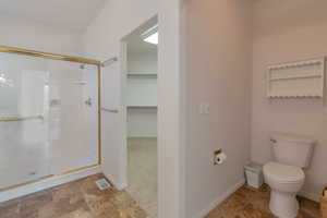 Full bathroom featuring a shower stall, stone finish floors, and a spacious closet