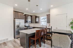 Kitchen with appliances with stainless steel finishes, dark brown cabinets, a center island, hanging light fixtures, and a breakfast bar area