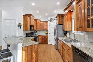 Kitchen with brown cabinets, black appliances, glass insert cabinets, light wood-style flooring, and crown molding