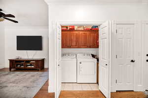 Laundry room with ornamental molding, cabinet space, ceiling fan, light wood-style flooring, and independent washer and dryer