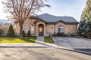 French country inspired facade featuring a front yard, stucco siding, and stone siding