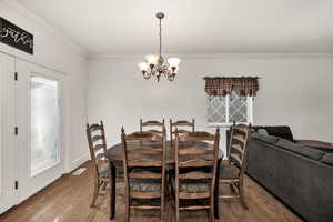 Dining room with wood finished floors, crown molding, and a chandelier