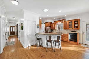 Kitchen featuring a breakfast bar, a peninsula, brown cabinetry, glass insert cabinets, and ornamental molding