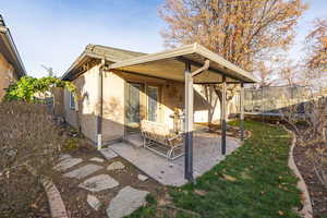 Back of property with a trampoline, a yard, a patio area, and stucco siding
