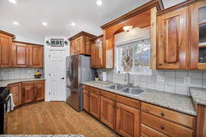 Kitchen with brown cabinets, light stone counters, tasteful backsplash, stainless steel fridge with ice dispenser, and ornamental molding