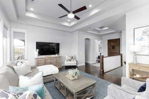 Living area featuring arched walkways, a tray ceiling, wood finished floors, recessed lighting, and ceiling fan