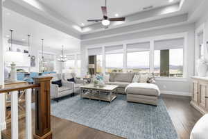 Living room featuring a chandelier, a tray ceiling, healthy amount of natural light, dark wood-type flooring, and recessed lighting