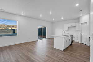 Kitchen with white cabinetry, an island with sink, light wood-style flooring, recessed lighting, and light stone countertops