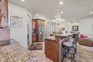 Kitchen featuring a breakfast bar, brown cabinetry, an island with sink, stainless steel fridge with ice dispenser, and hanging light fixtures