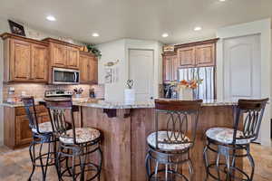Kitchen featuring brown cabinetry, stainless steel appliances, light stone counters, and recessed lighting