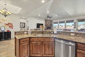 Kitchen with dishwasher, brown cabinets, dark stone counters, open floor plan, and a stone fireplace