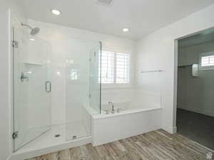 Full bath with a walk in closet, a stall shower, a garden tub, and wood finished floors