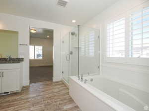Bathroom featuring a stall shower, a garden tub, vanity, a textured ceiling, and light wood-type flooring