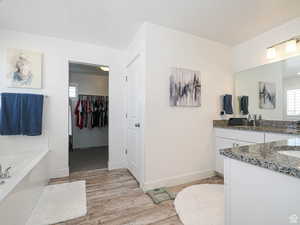 Full bath with a spacious closet, vanity, light wood-style floors, and a garden tub