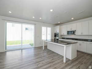 Kitchen featuring an island with sink, a breakfast bar, light wood-style flooring, white cabinetry, and dark stone countertops