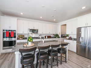 Kitchen featuring stainless steel appliances, a center island with sink, a breakfast bar, white cabinets, and recessed lighting