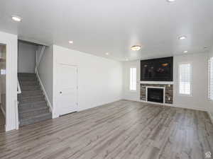 Unfurnished living room featuring stairway, light wood-style floors, a glass covered fireplace, a textured ceiling, and recessed lighting