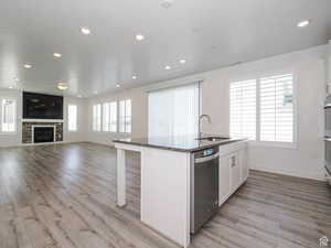 Kitchen featuring a kitchen island with sink, dark stone countertops, open floor plan, dishwasher, and light wood-style floors