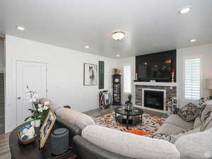 Living room featuring wood finished floors, a stone fireplace, recessed lighting, and a textured ceiling