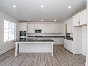 Kitchen featuring white cabinets, dark stone countertops, a kitchen island with sink, a breakfast bar, and recessed lighting