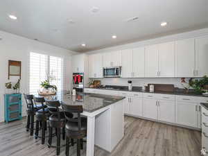 Kitchen with white cabinetry, dark stone counters, a kitchen island with sink, and recessed lighting