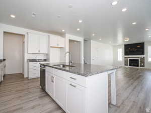 Kitchen featuring light wood-style floors, dark stone counters, a kitchen bar, open floor plan, and a kitchen island with sink