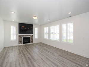Unfurnished living room with light wood finished floors, a glass covered fireplace, healthy amount of natural light, and recessed lighting