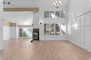 Unfurnished living room featuring light wood-style floors, a fireplace with flush hearth, high vaulted ceiling, and a chandelier
