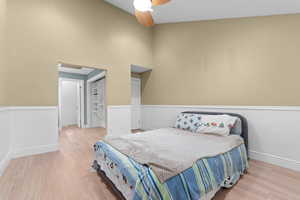 Bedroom featuring a walk in closet, light wood-type flooring, a ceiling fan, and a high ceiling