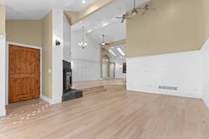 Unfurnished living room with high vaulted ceiling, a ceiling fan, a chandelier, light wood-type flooring, and a glass covered fireplace