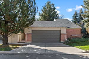 View of front of property with roof with shingles, brick siding, driveway, and a garage