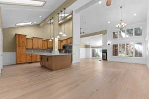 Kitchen with a ceiling fan, high vaulted ceiling, open floor plan, decorative light fixtures, and brown cabinets