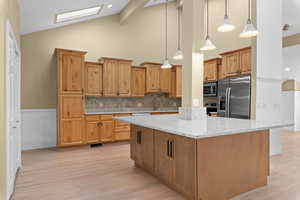 Kitchen with light stone countertops, hanging light fixtures, tasteful backsplash, stainless steel appliances, and a center island