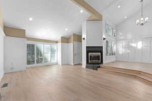 Unfurnished living room featuring high vaulted ceiling, light wood-style flooring, a glass covered fireplace, a chandelier, and recessed lighting