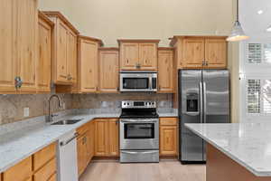 Kitchen featuring light stone countertops, appliances with stainless steel finishes, tasteful backsplash, pendant lighting, and light wood-type flooring