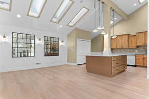 Kitchen with pendant lighting, open floor plan, a skylight, high vaulted ceiling, and light wood-style flooring