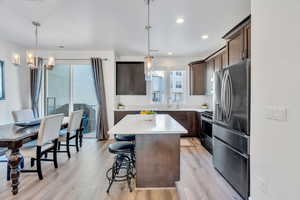 Kitchen with stainless steel appliances, dark brown cabinetry, a kitchen island, decorative light fixtures, and a chandelier
