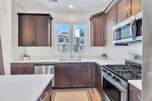 Kitchen featuring stainless steel appliances, dark brown cabinets, light wood-style floors, light stone counters, and recessed lighting