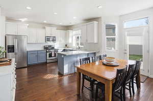 Kitchen with white cabinetry, stainless steel appliances, a peninsula, dark wood-style flooring, and light stone countertops