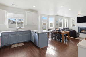Kitchen featuring open floor plan, a peninsula, a tile fireplace, dark wood-type flooring, and recessed lighting