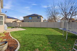 Fenced backyard with a trampoline, a patio area, and a residential view